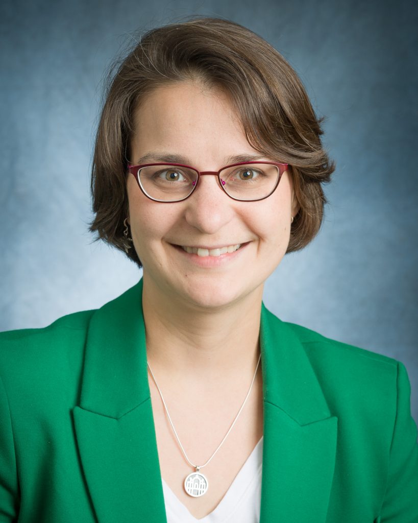 Headshot of Suzi White, a woman with short brown hair and glasses wearing a mallard green blazer.